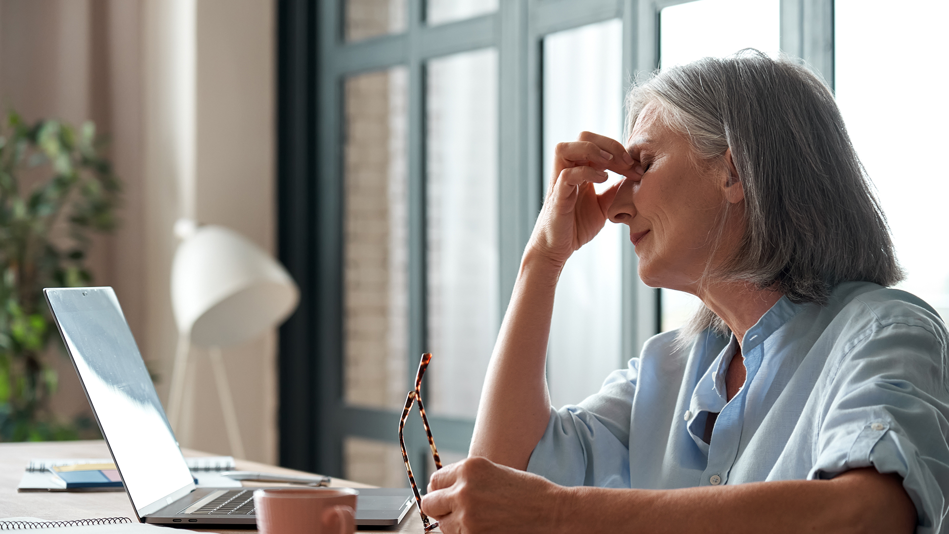 Tired old senior business woman taking off glasses suffers from eyestrain, stress