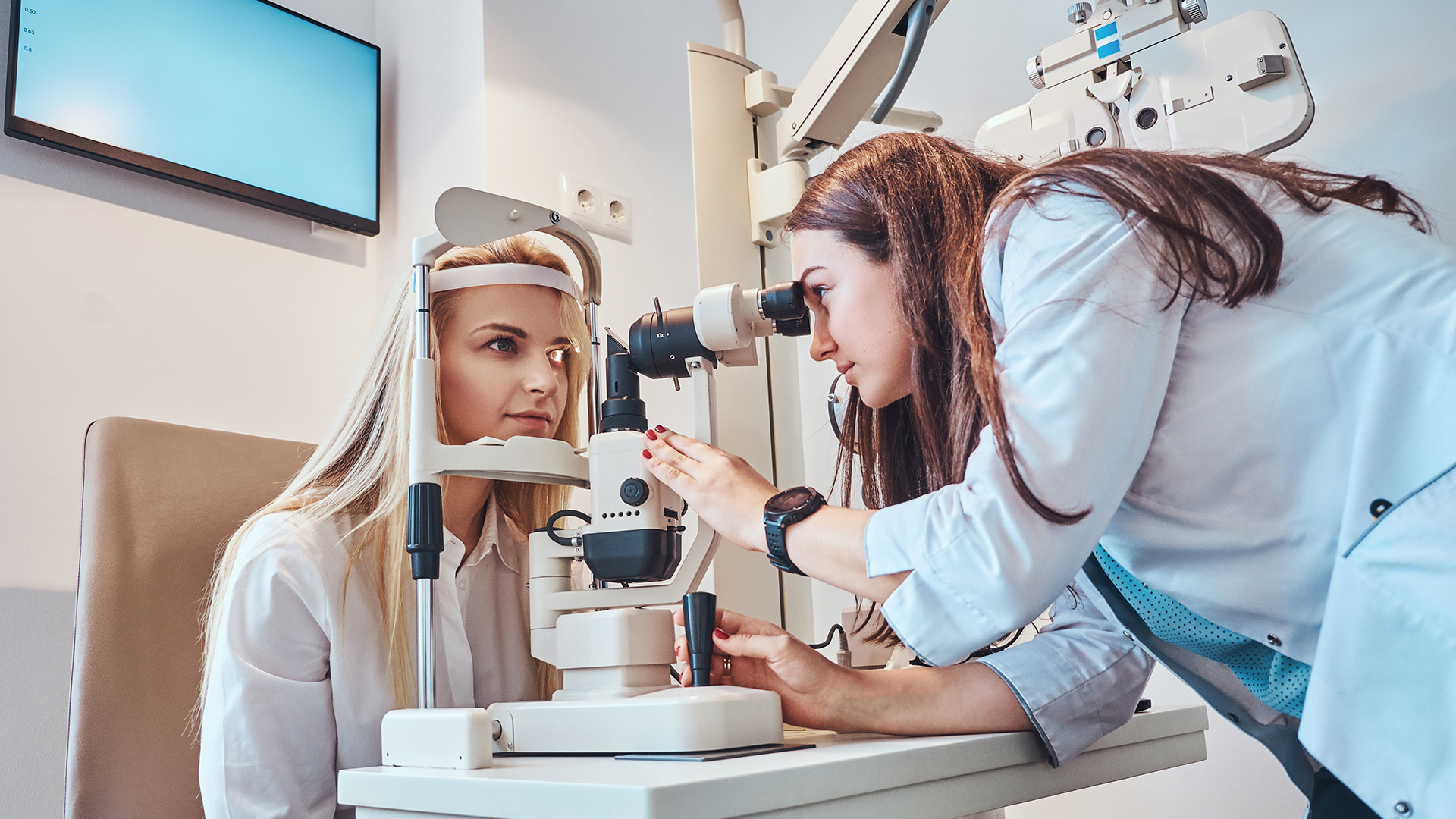 Two attractive females in oculist cabinet, one of them is a doctor, the second one is a patient.